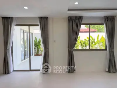 Spacious living room with large windows and sliding doors opening to a lush garden view.