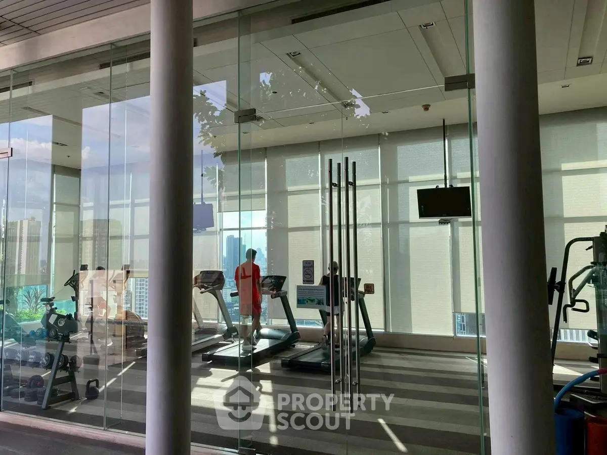 Modern gym with glass walls and city view, featuring treadmills and fitness equipment.