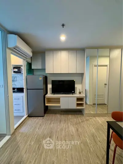 Modern living room with sleek design, featuring a TV, mirrored cabinets, and a glimpse of a stylish kitchen.