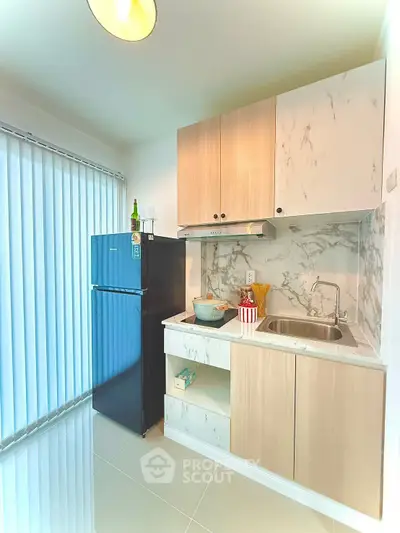 Modern kitchen with sleek cabinetry and marble backsplash, featuring a compact fridge and ample natural light.
