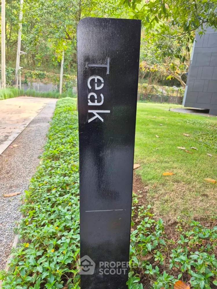 Modern garden with sleek black signpost labeled 'Teak' amidst lush greenery.