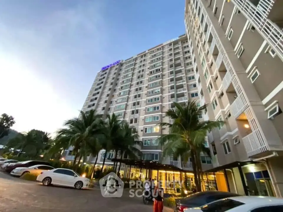Modern high-rise residential building with palm trees and parking area at dusk.
