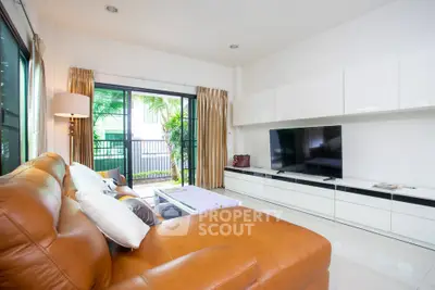 Spacious living room with modern decor and large TV, opening to a lush garden view.