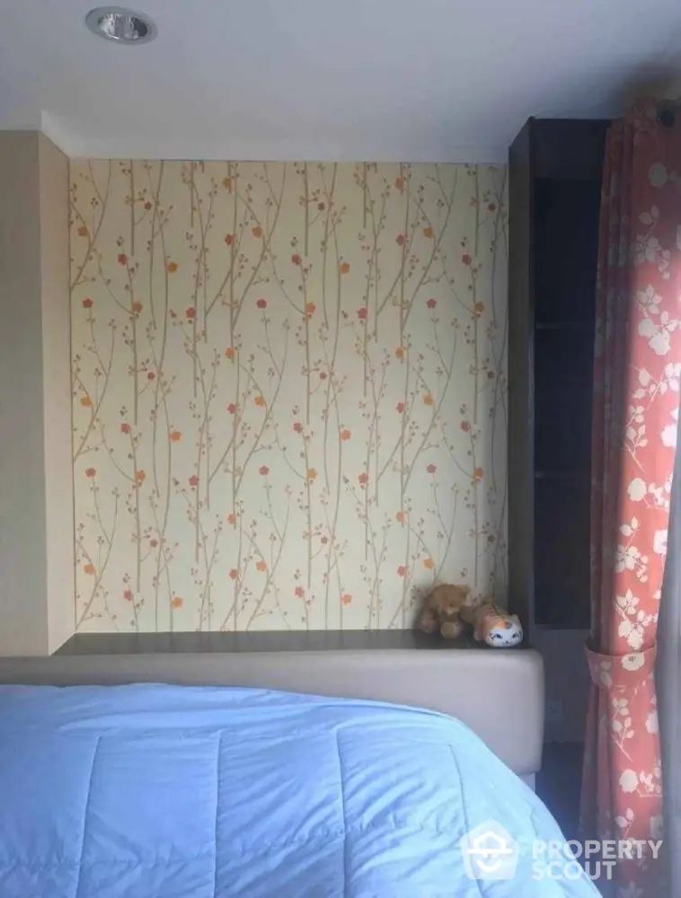 Cozy bedroom with floral wallpaper and plush toys on the shelf, perfect for relaxation.