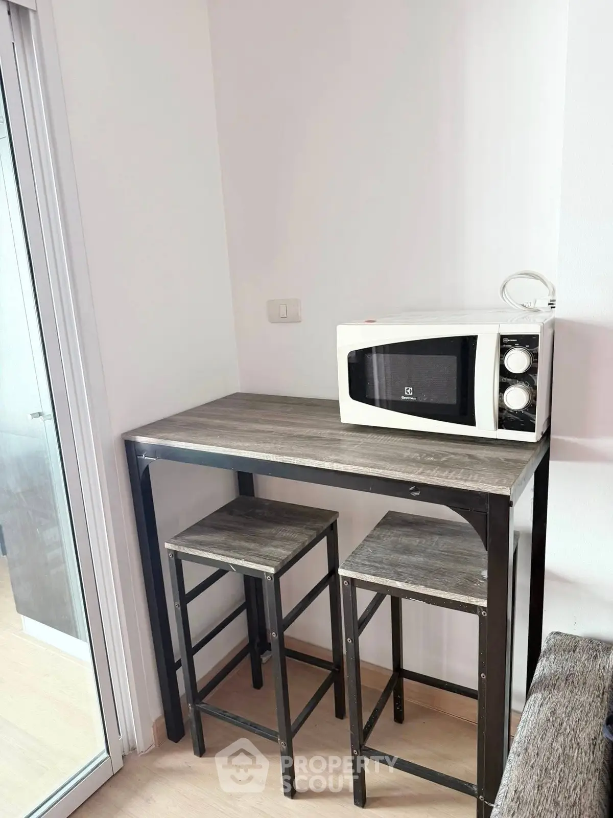 Compact kitchen corner with microwave and bar stools in modern apartment.