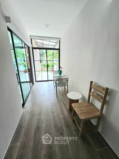 Bright hallway with wooden flooring and glass doors leading to a garden view.