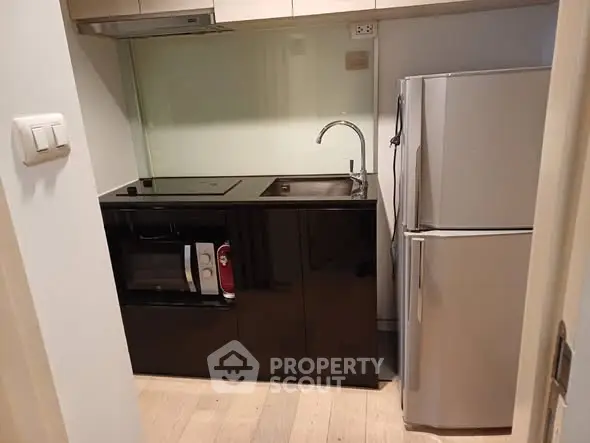 Compact modern kitchen with sleek black cabinetry and stainless steel appliances.
