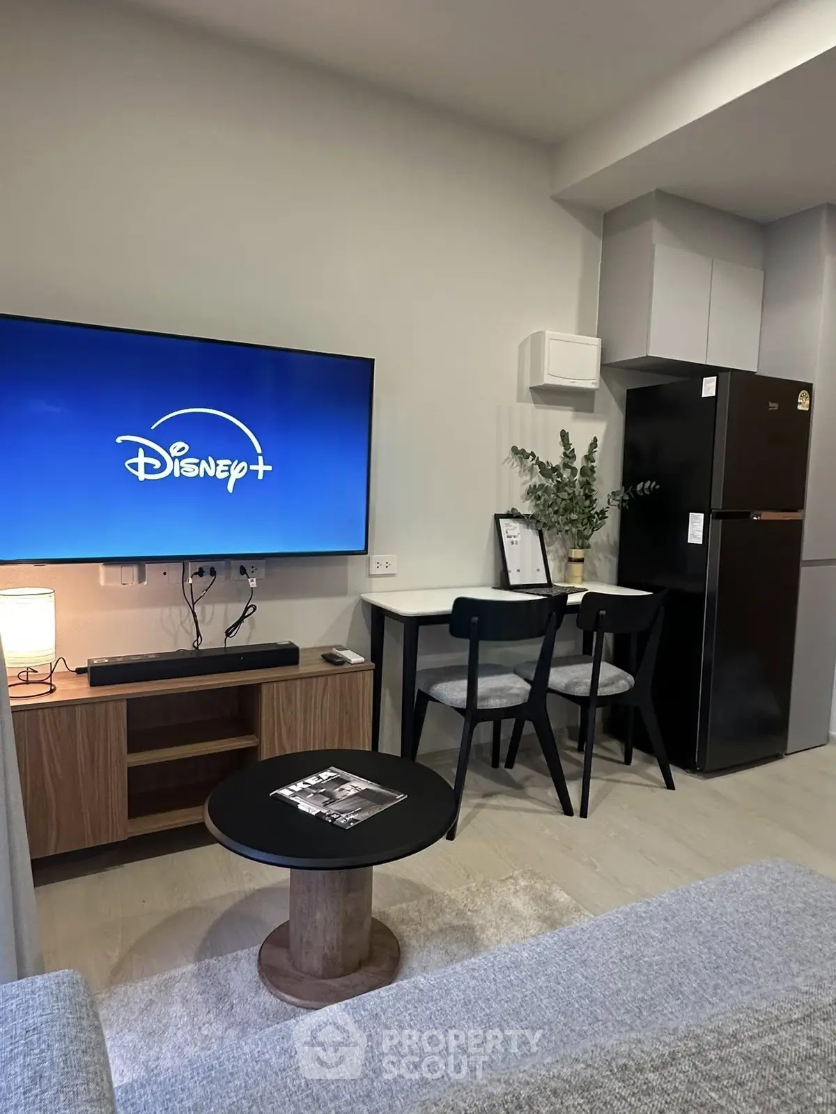 Modern living room with sleek furniture and entertainment setup, featuring a large TV and cozy dining area.