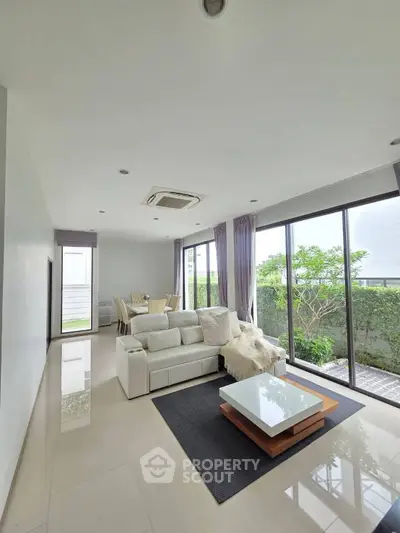 Spacious modern living room with large windows and garden view, featuring elegant furniture and natural light.