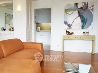 Modern living room with leather sofa and abstract art, open to a stylish kitchen.