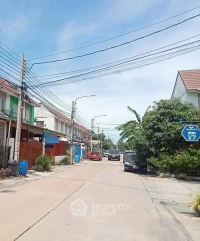 Charming residential street with townhouses and lush greenery under a clear blue sky.