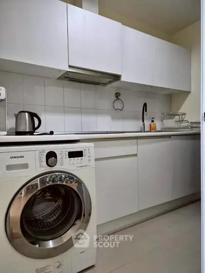 Modern kitchen with sleek white cabinets and built-in washing machine.