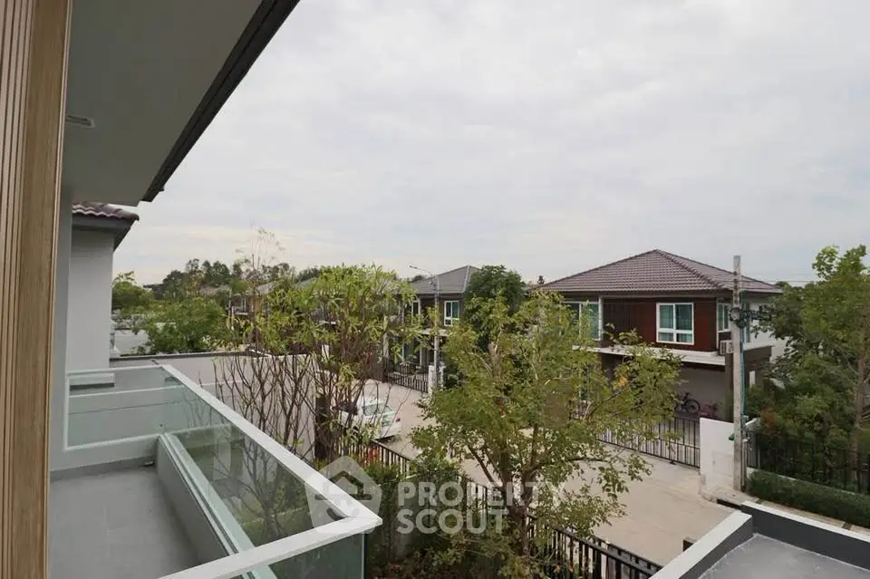 Charming suburban view from a modern balcony overlooking a quiet residential street with lush greenery.