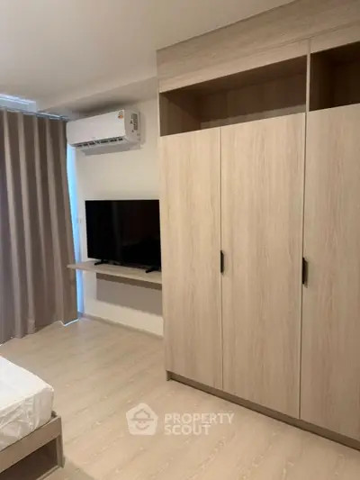 Modern bedroom with sleek wardrobe and mounted TV, featuring air conditioning and elegant curtains.