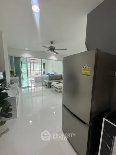 Modern open-plan living room with sleek kitchen and stainless steel fridge, bright and airy ambiance.