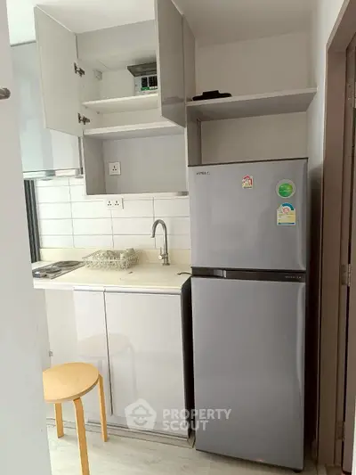 Compact kitchen with modern fridge and open shelving in a cozy apartment.