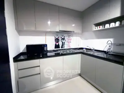 Modern kitchen with sleek cabinetry and black countertops, featuring a microwave and stainless steel sink.