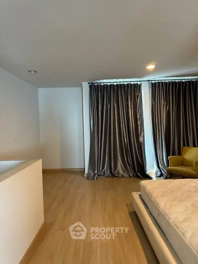 Spacious bedroom with elegant curtains and wooden flooring, featuring a cozy armchair and modern bed frame.