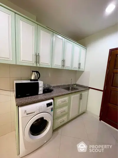 Modern kitchen with washing machine and microwave, sleek cabinetry, and ample counter space.