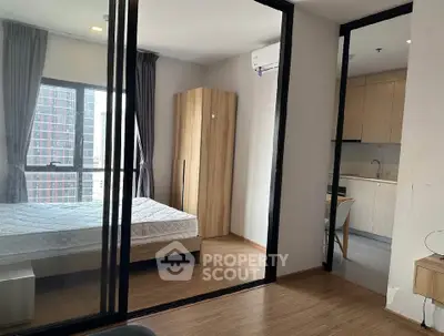 Modern apartment with bedroom and kitchen, featuring large windows and sleek wooden flooring.