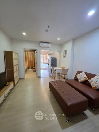 Modern living room with brown leather sofa and open layout leading to kitchen and bedroom.