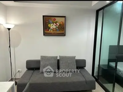 Modern living room with gray sofa and floral painting, adjacent to glass-walled bedroom.