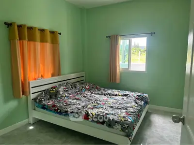 Cozy bedroom with colorful bedding and green walls, featuring a window with a view.