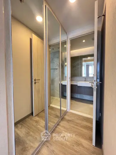 Modern hallway with mirrored closet doors leading to a stylish bathroom with elegant fixtures.