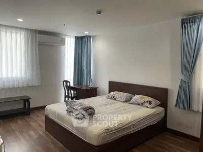 Spacious bedroom with wooden flooring and natural light