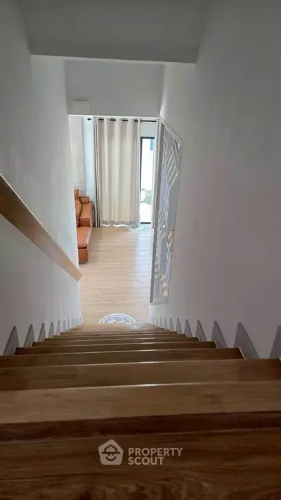 Modern staircase leading to a cozy living room with wooden flooring and natural light.
