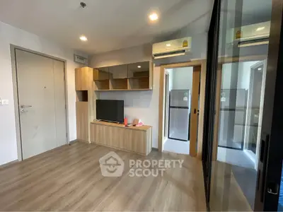 Modern living room with sleek wooden flooring and built-in TV unit, adjacent to a compact kitchen area.
