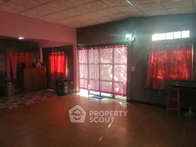 Spacious living room with natural light and tiled flooring, featuring vibrant red curtains and cozy ambiance.