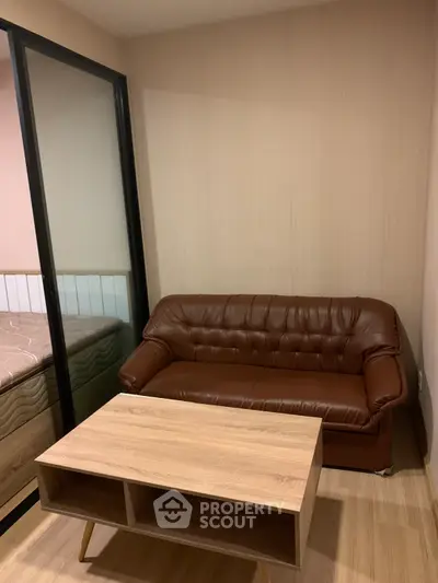 Cozy living room with brown leather sofa and wooden coffee table, adjacent to a bedroom.