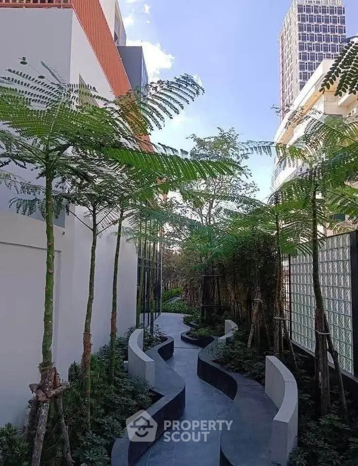 Modern building exterior with lush garden pathway and tall trees, offering a serene urban oasis.