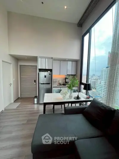 Modern living room with open kitchen and city view, featuring sleek furniture and large windows.