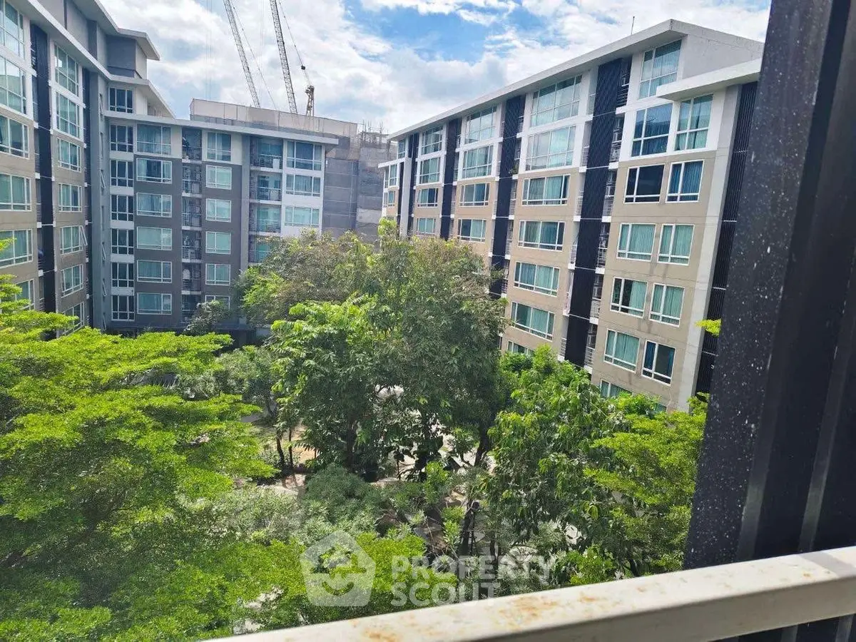 Modern apartment complex with lush green courtyard and construction cranes in the background.