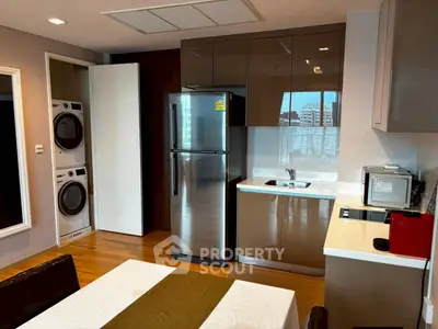 Modern kitchen with stainless steel appliances and stacked washer-dryer in sleek apartment.