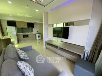 Modern living room with open kitchen, featuring sleek furniture and appliances.