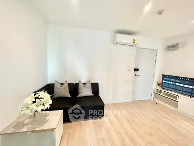 Modern living room with sleek black sofa, wall-mounted TV, and air conditioning in a bright, minimalist design.