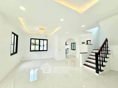 Spacious modern living room with elegant staircase and bright natural lighting.