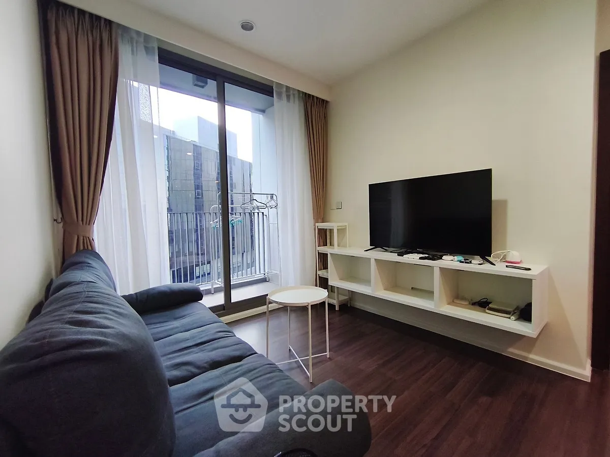 Modern living room with large window and balcony access, featuring a sleek TV setup and comfortable seating.