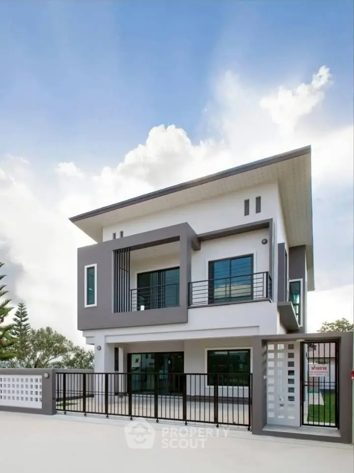 Modern two-story house with sleek design and spacious balcony under a clear blue sky.