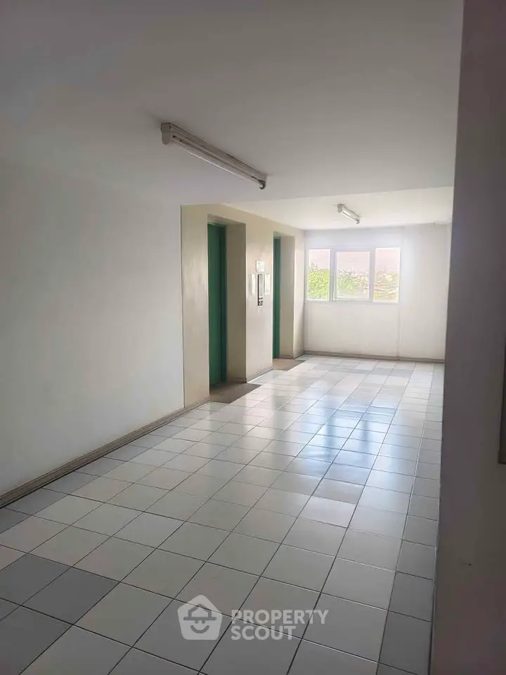 Bright and spacious building corridor with elevator access and tiled flooring.