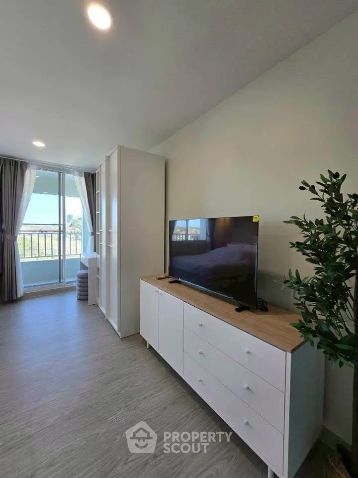 Modern living room with TV, stylish furniture, and balcony view in a bright apartment.