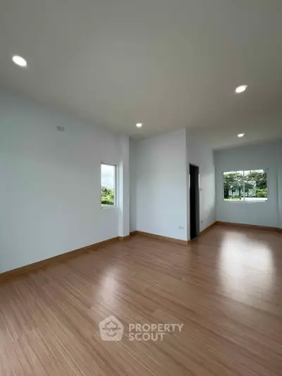 Spacious empty room with wooden flooring and large windows offering natural light.