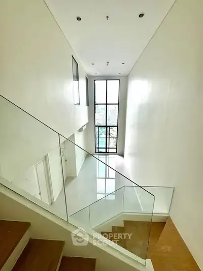 Spacious modern staircase with glass railing and large window view