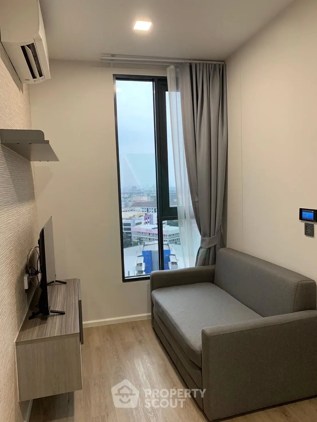 Modern living room with city view, featuring a sleek gray sofa and wall-mounted TV, perfect for urban living.