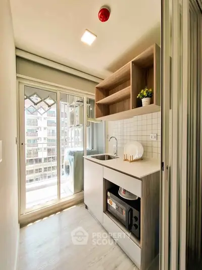 Modern compact kitchen with balcony view, featuring sleek cabinetry and built-in appliances in a bright setting.