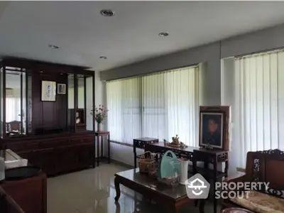 Elegant living room with traditional wooden furniture and large windows with blinds, creating a cozy atmosphere.