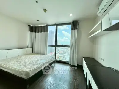 Modern bedroom with large window offering city view, featuring sleek furniture and hardwood floors.